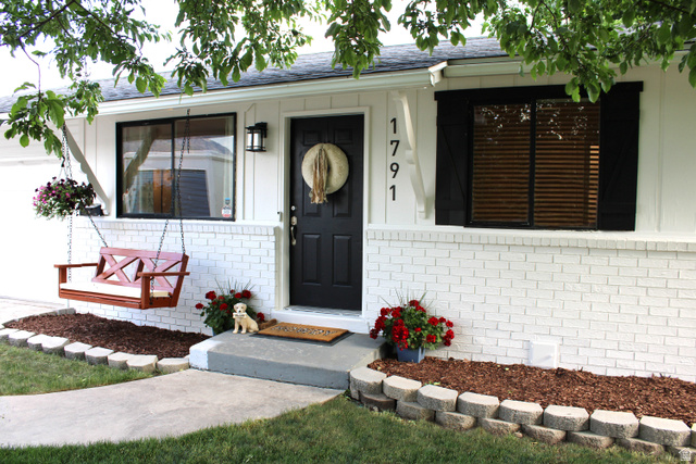 Charming façade featuring a white painted brick foundation, contrasting dark entry door, and black window frames with matching shutters