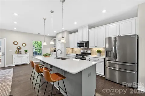 a kitchen with stainless steel appliances a refrigerator a stove a sink a center island and chairs