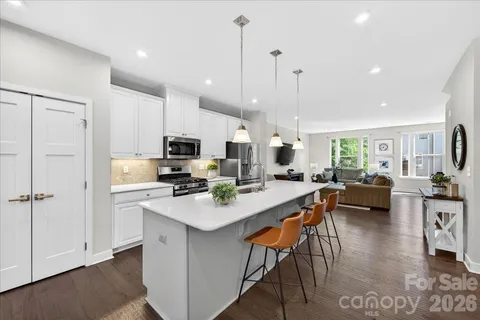 a kitchen with stainless steel appliances kitchen island granite countertop a stove top oven a sink a dining table and chairs with wooden floor