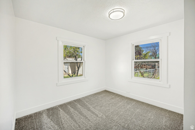 712 9th Street Ogden, UT 84404 - Photo 7 of 15 Bright interior space featuring two windows, neutral wall tones, textured gray carpeting, white baseboards, and a contemporary ceiling light fixture