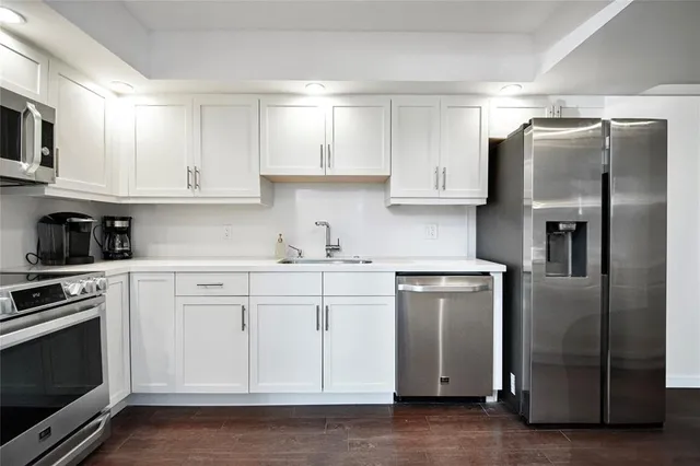 a kitchen with stainless steel appliances granite countertop a refrigerator a stove a sink and white cabinets with wooden floor