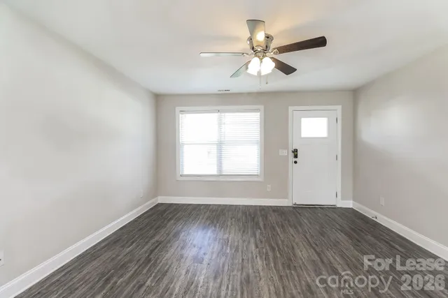 an empty room with wooden floor chandelier fan and windows