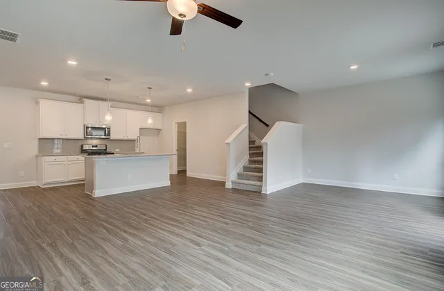 an empty room with wooden floor kitchen view and a window