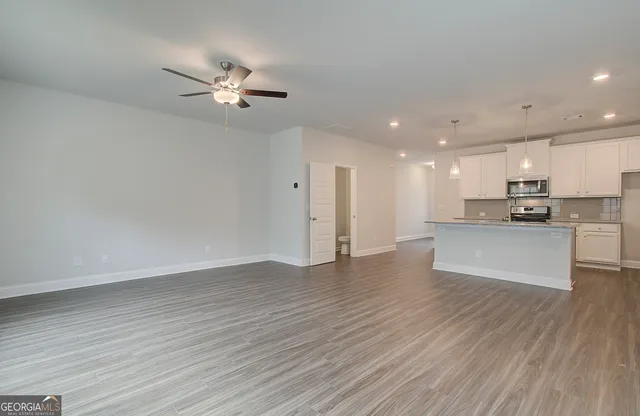 a view of an empty room with wooden floor and a kitchen view