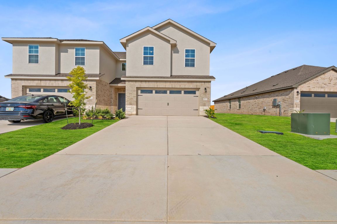 View of front facade with a front lawn, stucco siding, concrete driveway, and brick siding