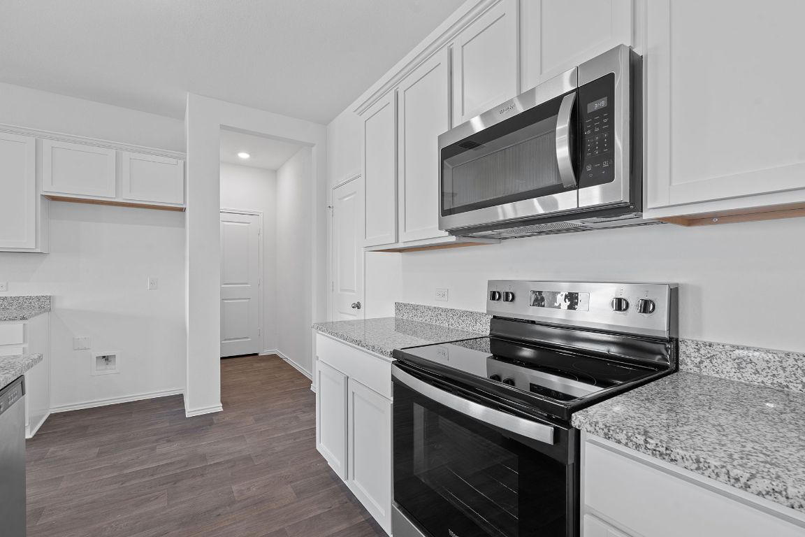 18500 B Empire Path Manor, TX 78653 - Photo 6 of 31 Kitchen featuring appliances with stainless steel finishes, light stone countertops, white cabinets, dark wood finished floors, and recessed lighting