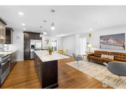 a living room with stainless steel appliances kitchen island granite countertop a refrigerator a sink dishwasher and a dining table with wooden floor