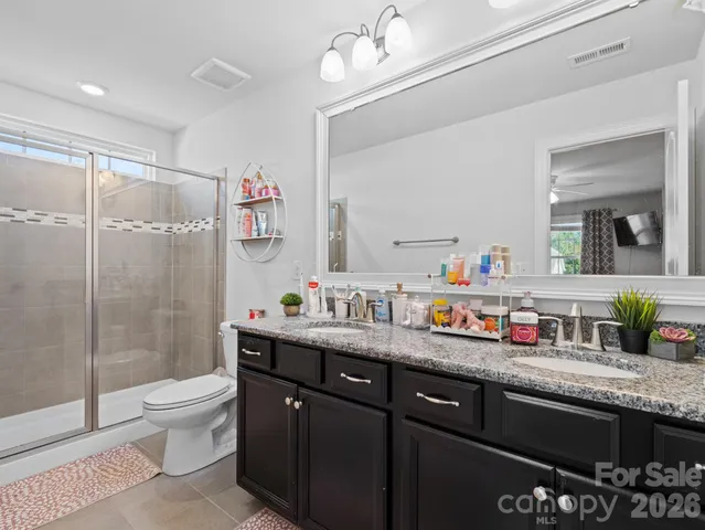 a bathroom with a granite countertop sink a toilet a mirror a vanity and shower