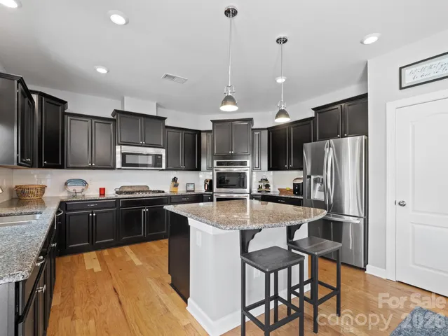 a kitchen with kitchen island granite countertop a stove top oven a sink dishwasher a refrigerator and white cabinets with wooden floor