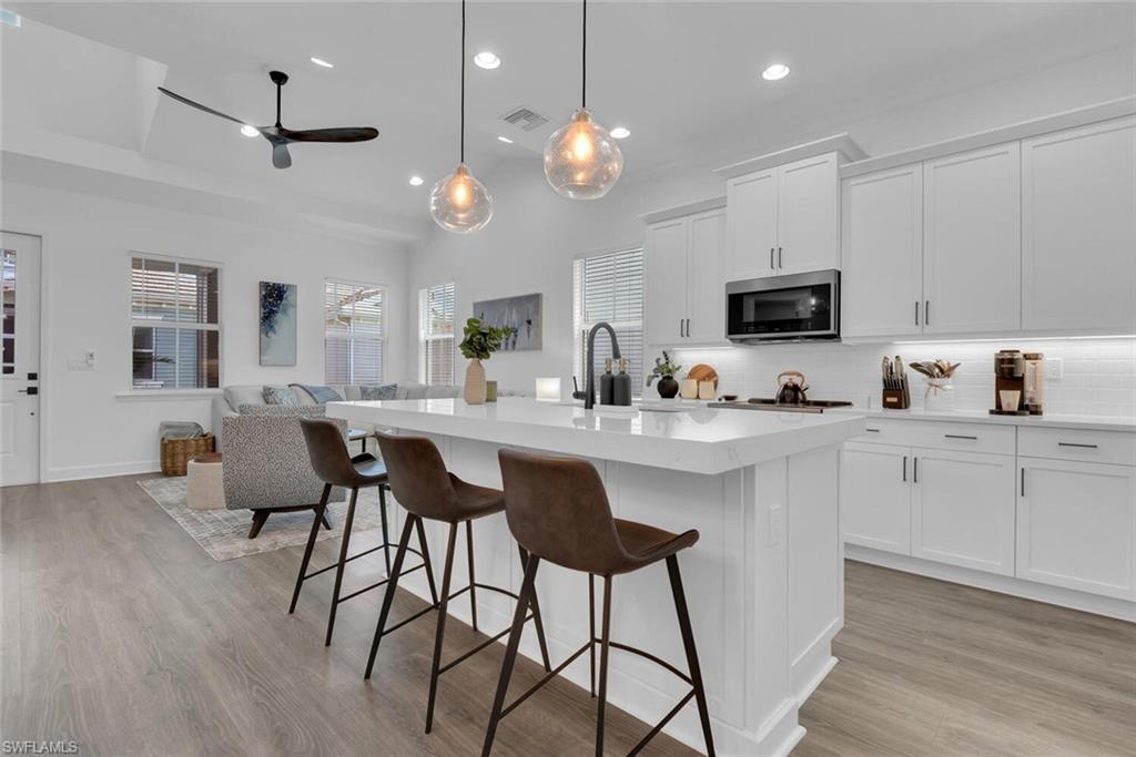 7242 Saona Court Naples, FL 34113 - Photo 34 of 34 a kitchen with stainless steel appliances kitchen island granite countertop a sink a microwave a dining table and chairs with wooden floor