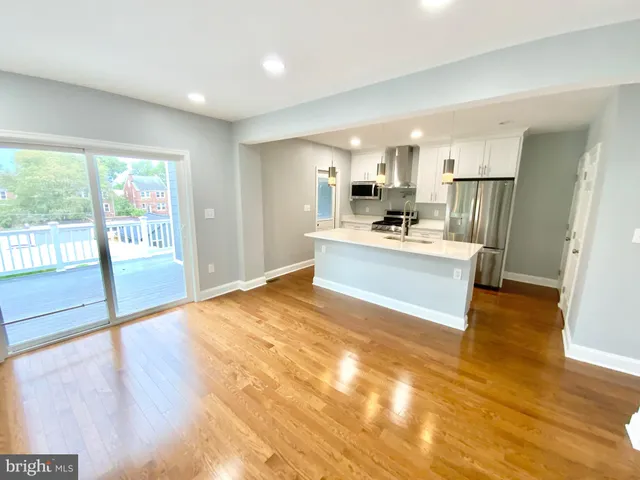 a living room with stainless steel appliances kitchen island granite countertop a refrigerator stove a sink and dishwasher with wooden floor