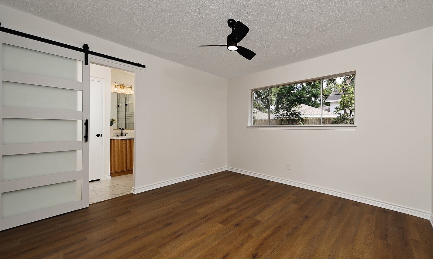 19410 Craigchester Lane Spring, TX 77388 - Photo 26 of 32 Spacious primary suite has window overlooking backyard and the addition of a custom sliding 5-lite barn door with modern black hardware takes this room to a different level in elegance and high end style.