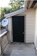 6001 Reims Road, Unit 1202 Houston, TX 77036 - Photo 11 of 16 This photo shows an outdoor entrance to a home with a black door, beige siding, and a railing. There is a satellite dish attached to the railing, and trees are visible in the background.