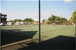 6001 Reims Road, Unit 1202 Houston, TX 77036 - Photo 15 of 16 The photo shows a fenced tennis court adjacent to a parking area, surrounded by trees and a building, ideal for recreational activities.