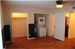 6001 Reims Road, Unit 1202 Houston, TX 77036 - Photo 5 of 16 This photo shows a room with hardwood flooring, a ceiling light, and a compact laundry area with a stacked washer and dryer. There are two open doorways leading to a closet and another room.