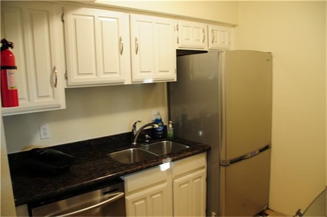 6001 Reims Road, Unit 1202 Houston, TX 77036 - Photo 8 of 16 This compact kitchen features white cabinetry, a dark granite countertop, stainless steel appliances, and a sleek fridge, offering a modern and efficient space.