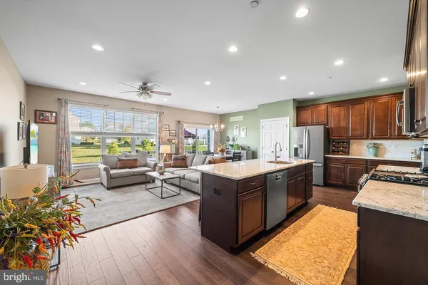 a kitchen with stainless steel appliances granite countertop wooden cabinets a sink a stove a refrigerator and a dining table with wooden floor