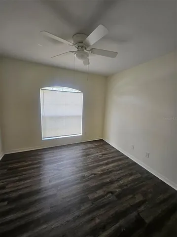 an empty room with wooden floor fan and windows