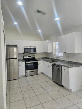 a kitchen with granite countertop a refrigerator and white cabinets