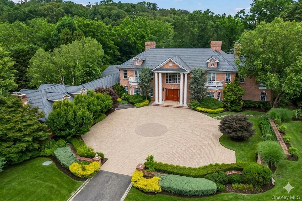 660 Chicken Valley Road Locust Valley, NY 11560 - Photo 2 of 48 Brick exterior with a prominent portico featuring white columns, a circular paved driveway, and established landscape beds
