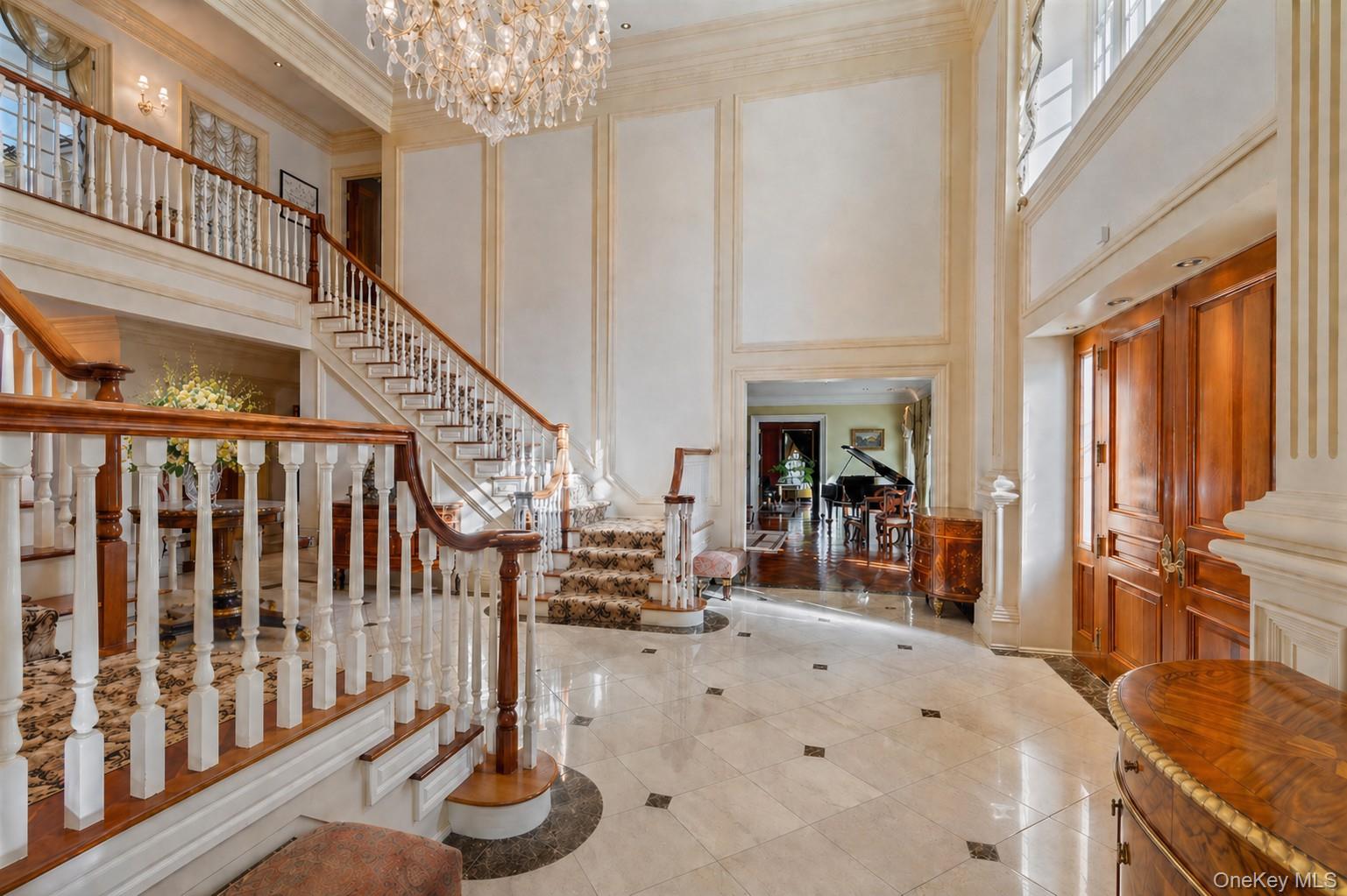 660 Chicken Valley Road Locust Valley, NY 11560 - Photo 5 of 48 Grand entry foyer featuring a sweeping staircase with detailed balusters and wood handrails, marble flooring with accent inlays, and a multi-tiered crystal chandelier