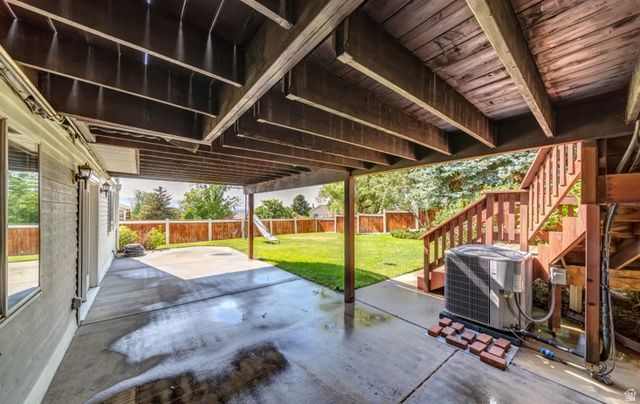 1273 Grayson Court Sandy, UT 84094 - Photo 27 of 27 Covered concrete patio with exposed wood joists and support beams, overlooking a fenced backyard with mature landscaping and a wooden staircase