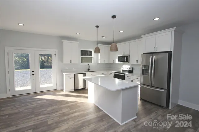 a kitchen with stainless steel appliances granite countertop a refrigerator a sink dishwasher a stove and white cabinets with wooden floor