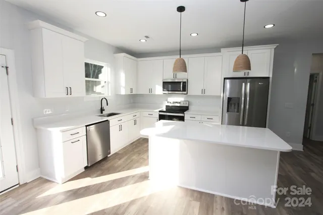 a large kitchen with stainless steel appliances granite countertop a stove a sink a microwave a refrigerator and white cabinets with wooden floor