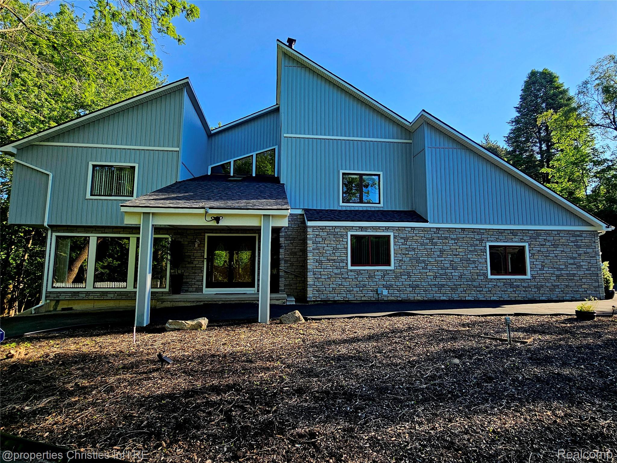 1830 Lone Pine Road Bloomfield Hills, MI 48302 - Photo 2 of 49 Contemporary exterior featuring a stone facade, vertical siding, a covered entry, multiple window styles, and an asphalt driveway