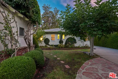a view of a white house next to a yard with a tree