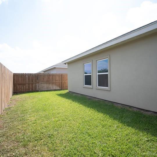 3052 Briggs Road, Unit C Weslaco, TX 78596 - Photo 16 of 16 Spacious backyard featuring a manicured lawn, full wood fencing, and a stucco exterior with two windows