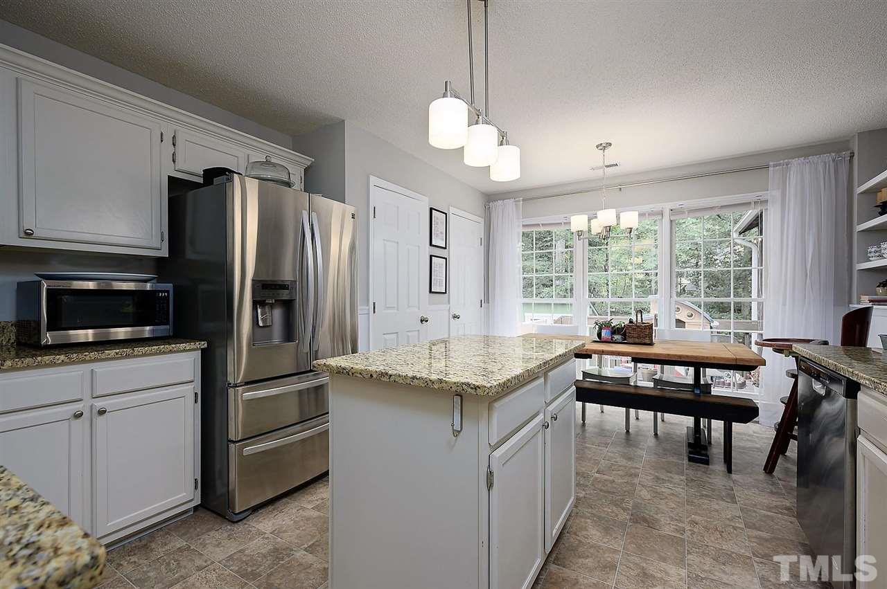 11917 North Exeter Way Raleigh, NC 27613 - Photo 8 of 18 a kitchen with kitchen island granite countertop a stove a refrigerator a sink a dining table and chairs with wooden floor