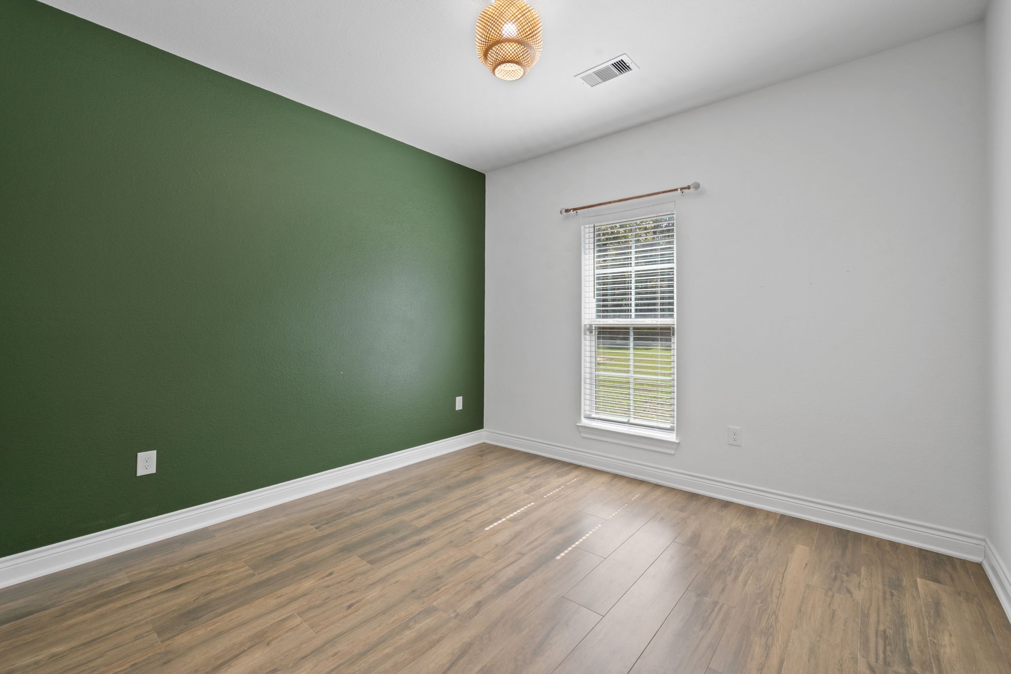 7815 Timber Switch Road Cleveland, TX 77328 - Photo 12 of 39 Bright room with a striking green accent wall, modern wood flooring, and ample natural light from a large window.