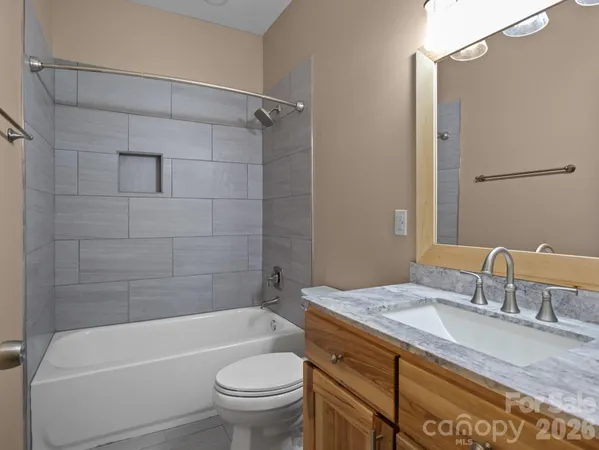 a bathroom with a granite countertop bathtub shower sink vanity mirror and toilet