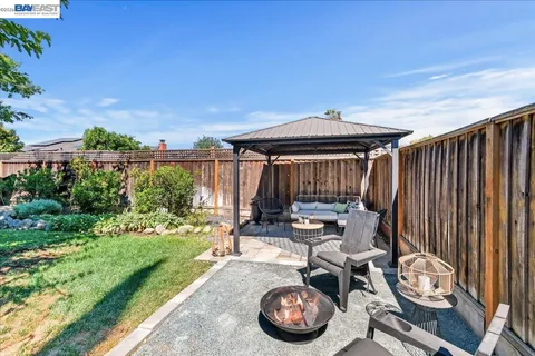 a backyard of a house with table and chairs plants and a large tree