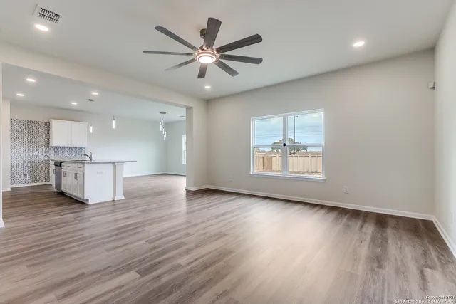 an empty room with wooden floor a ceiling fan and windows