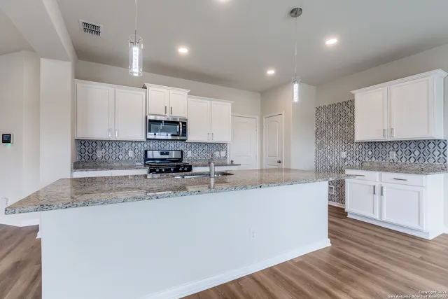 a large kitchen with stainless steel appliances granite countertop a stove a sink a refrigerator a microwave and cabinets