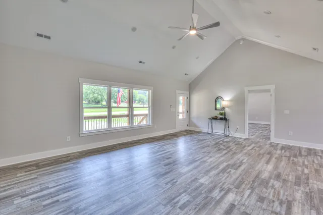 an empty room with wooden floor chandelier fan and windows