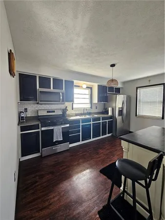 a kitchen with stainless steel appliances a refrigerator a stove a sink dishwasher with a dining table and chairs with wooden floor