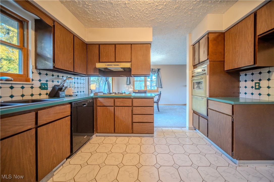 1206 Dussel Road Kent, OH 44240 - Photo 16 of 28 Kitchen with backsplash, brown cabinets, a peninsula, dishwasher, and a textured ceiling