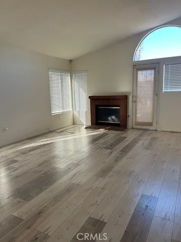 an empty room with wooden floor fireplace and windows
