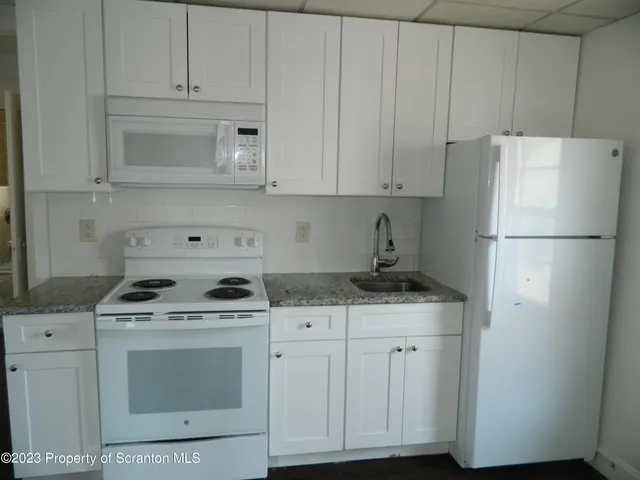 a kitchen with granite countertop white cabinets and refrigerator