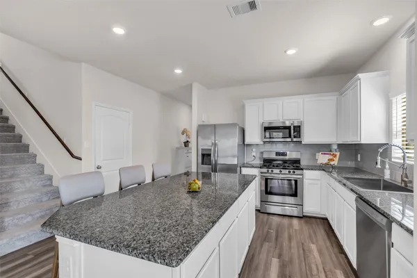 a kitchen with stainless steel appliances granite countertop a stove top oven a sink dishwasher a refrigerator and cabinets with wooden floor