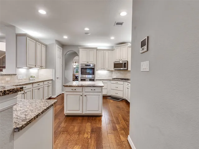 a kitchen with stainless steel appliances granite countertop a stove top oven a sink dishwasher and a refrigerator with wooden floor