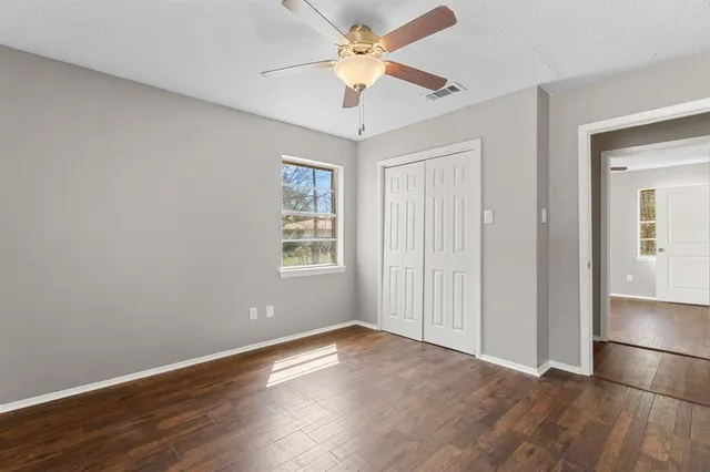 an empty room with wooden floor chandelier fan and windows