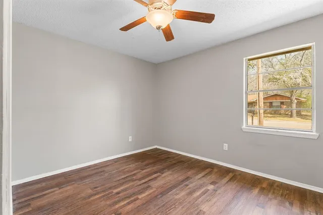an empty room with wooden floor chandelier fan and windows