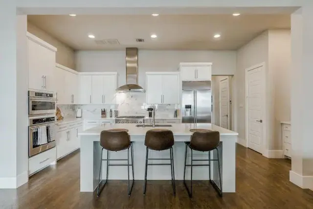 a kitchen with stainless steel appliances granite countertop a stove a refrigerator a kitchen island and chairs with wooden floor