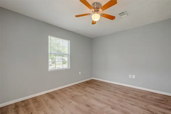 an empty room with wooden floor fan and windows
