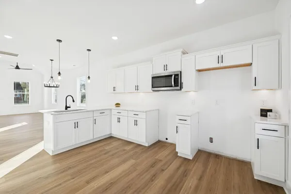 a large white kitchen with cabinets stainless steel appliances a sink and wooden floor