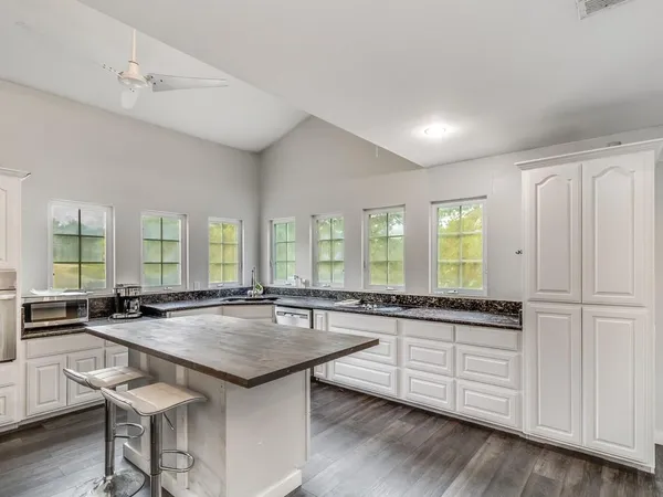 a large kitchen with granite countertop a sink and white cabinets with wooden floor